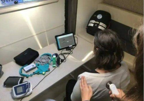 Téléconsultation en mobilité Professionnel formé au dispositif portatif de télémédecine en mobilité qui osculte une patiente de dos avec le stéthoscope connecté